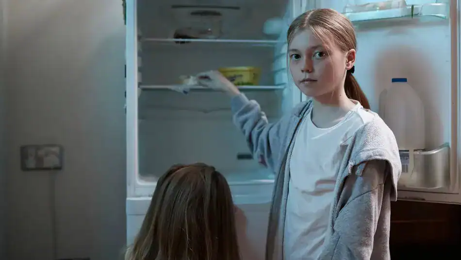 Young girl looking at the camera inside a refrigerator.