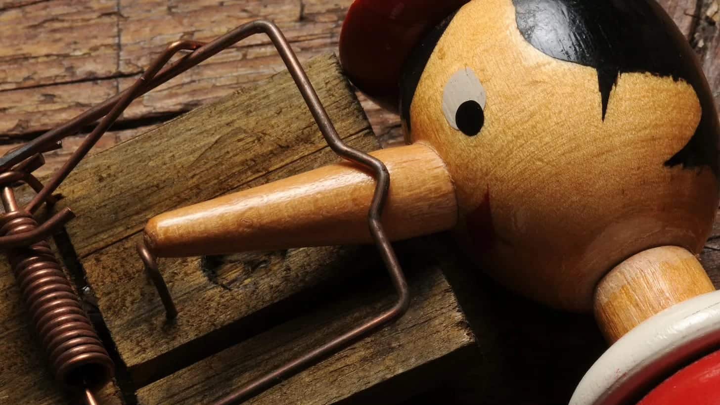 Wooden puppet with a long nose and metal legs on a rustic wooden surface.